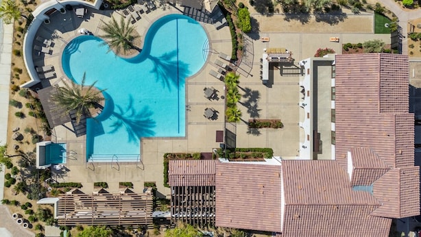 Eine Vogelperspektive zeigt einen luxuriösen Urlaubsort mit einem großen Schwimmbecken, Liegestühlen und einem überdachten Bereich mit Tischen und Stühlen.