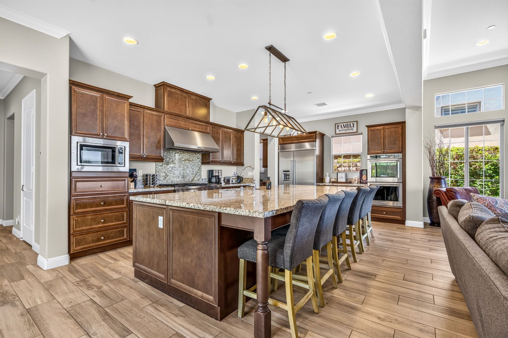 A spacious kitchen with a large island, wooden cabinets, stainless steel appliances, and a bar area with stools.