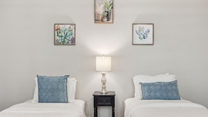 Ein Hotelzimmer mit zwei Betten, einem Nachttisch mit Lampe und drei gerahmten Blumenbildern an der Wand.
