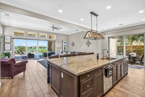 A spacious kitchen with a large island, modern appliances, and a view to an outdoor patio area. - Exclusive Escape: Poolside Luxury near Scenic Golf (La Quinta)