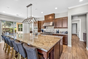 A spacious kitchen with a large island, wooden cabinets, and a modern stainless steel range hood.