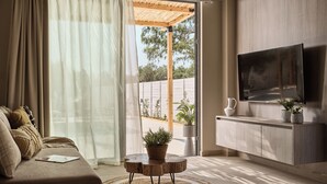 A modern living room with a sofa, a coffee table, a TV, and a sliding glass door leading to an outdoor area. - Liostasi Village  (Zakynthos)