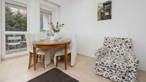 A dining area with a round table, chairs, a vase with flowers, and a chair with a floral pattern. - Spacious Apartment for 6 persons | 2 Bedrooms | Balcony (Warszawa)