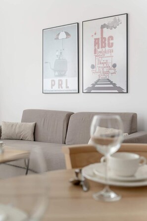 Un salon moderne avec un canapé gris, une table basse sur laquelle se trouve un verre de vin, et deux affiches encadrées accrochées au mur.