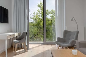 Une chambre moderne équipée d’un bureau, de deux chaises, d’une grande fenêtre donnant sur la verdure et d’une lampe.