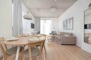 Un salon moderne avec une table à manger ronde en bois, des canapés gris et un grand miroir au mur.