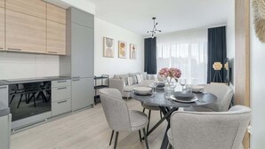 A modern kitchen with grey cabinets, a dining area with a round table set for four, and a sofa in the background.