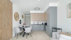 A modern kitchen with grey cabinets, a dining area with a round table and chairs, and a grey sofa.