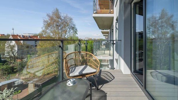 A balcony with a wicker chair and a table, overlooking a residential area.