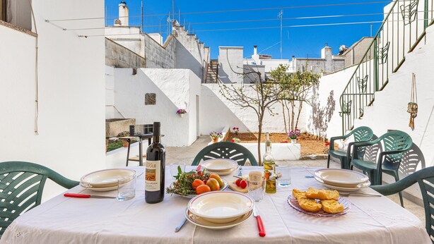 A table set for dining outdoors with plates, cutlery, and a bottle of wine, surrounded by green chairs. - 3836 Da Donatuccia by Barbarhouse (Presicce-Acquarica)