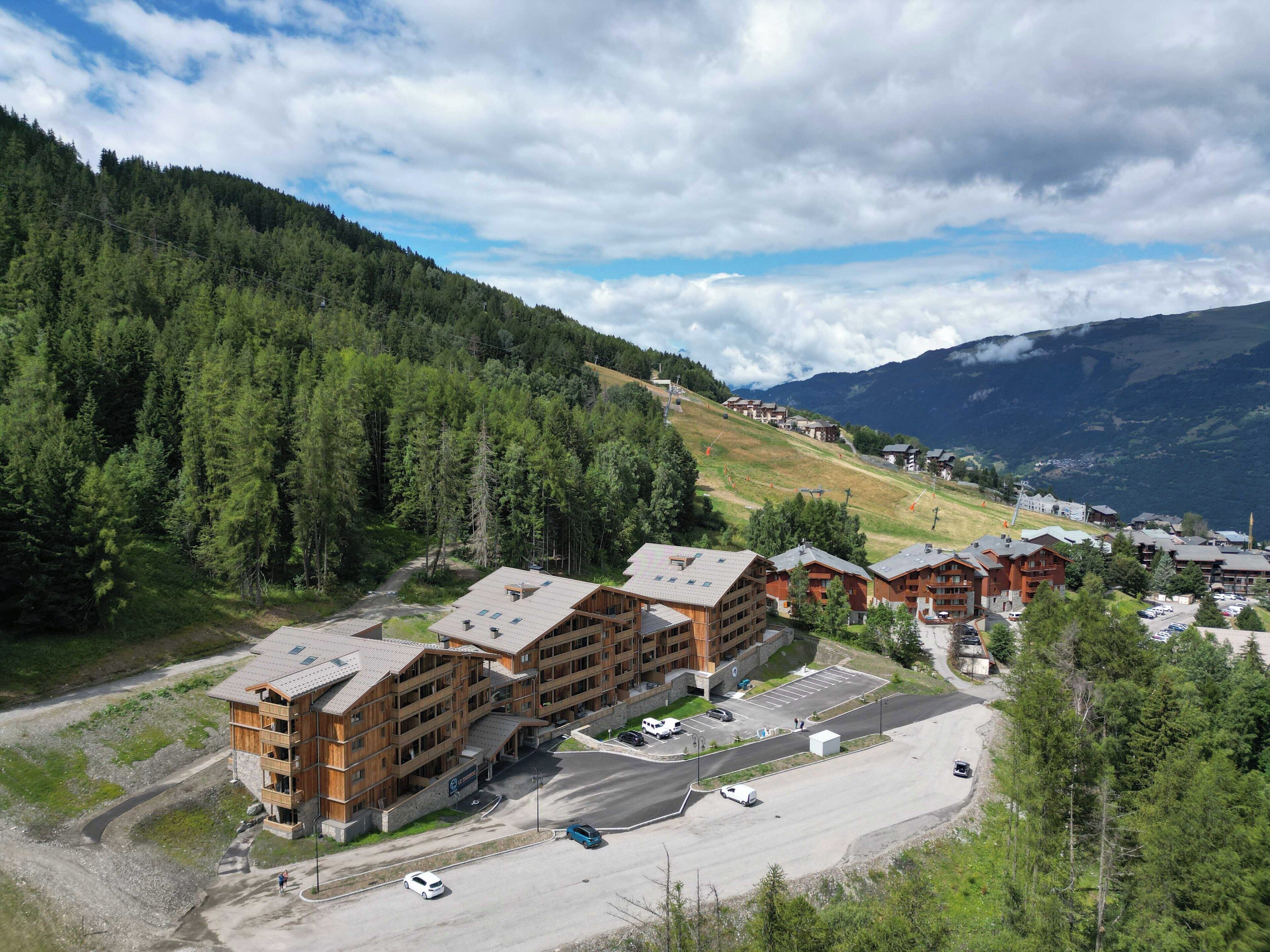 A lodge with multiple wooden buildings, a parking area, and a mountainous backdrop.
