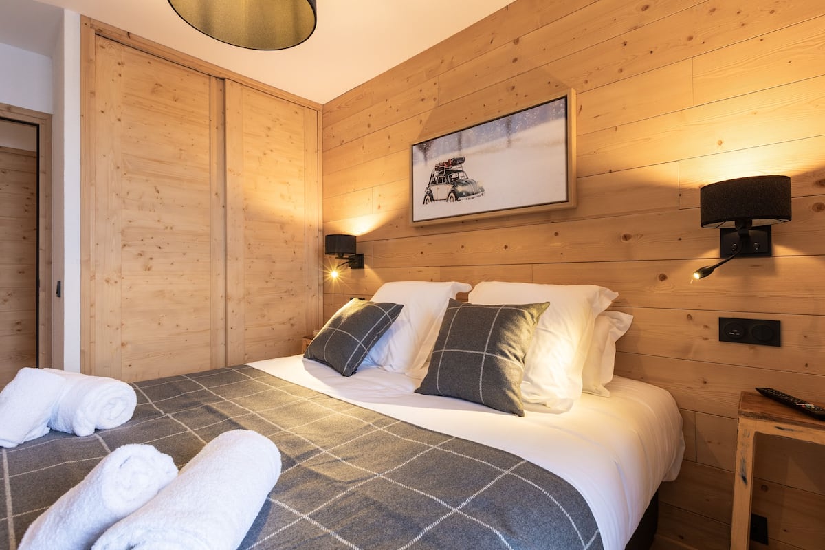 Ein Zimmer mit Holzwandverkleidung, einem Bett, zwei Wandlampen und einem gerahmten Bild an der Wand.