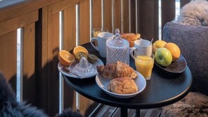 Une table de petit-déjeuner avec des croissants, des fruits et du jus, placée sur un balcon donnant sur un paysage montagneux enneigé.