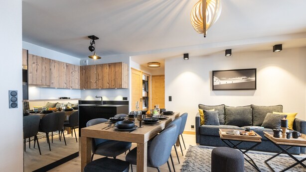 Een moderne keuken met houten kastjes, een eethoek met een houten tafel en stoelen, en een zithoek met een bank en salontafel.