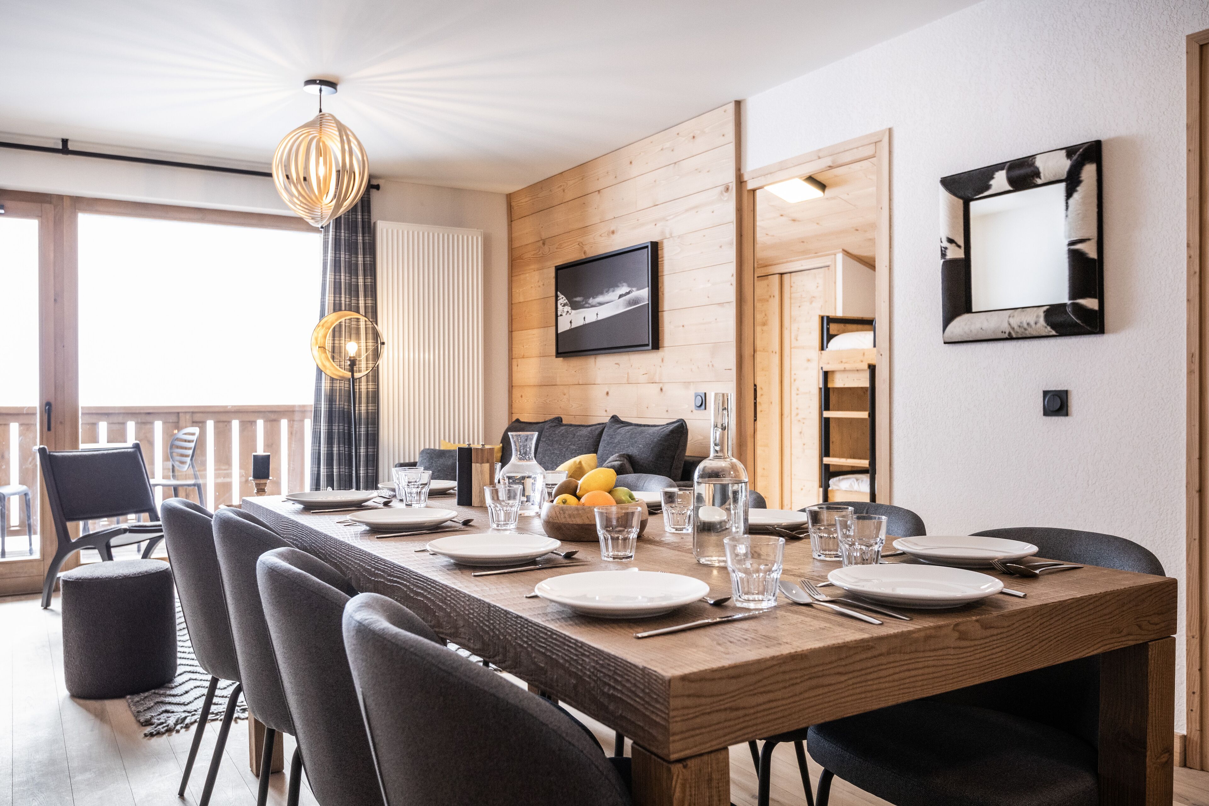A dining area with a wooden table set for four, chairs, and a large window with curtains.