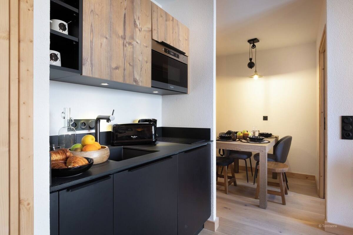 Eine kompakte Küche mit schwarzer Arbeitsplatte, einem Toaster und einem Holzschrank über der Mikrowelle.