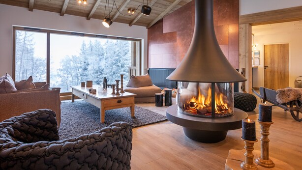 Un salon chaleureux avec une cheminée, des meubles en bois et une grande fenêtre donnant sur la forêt.