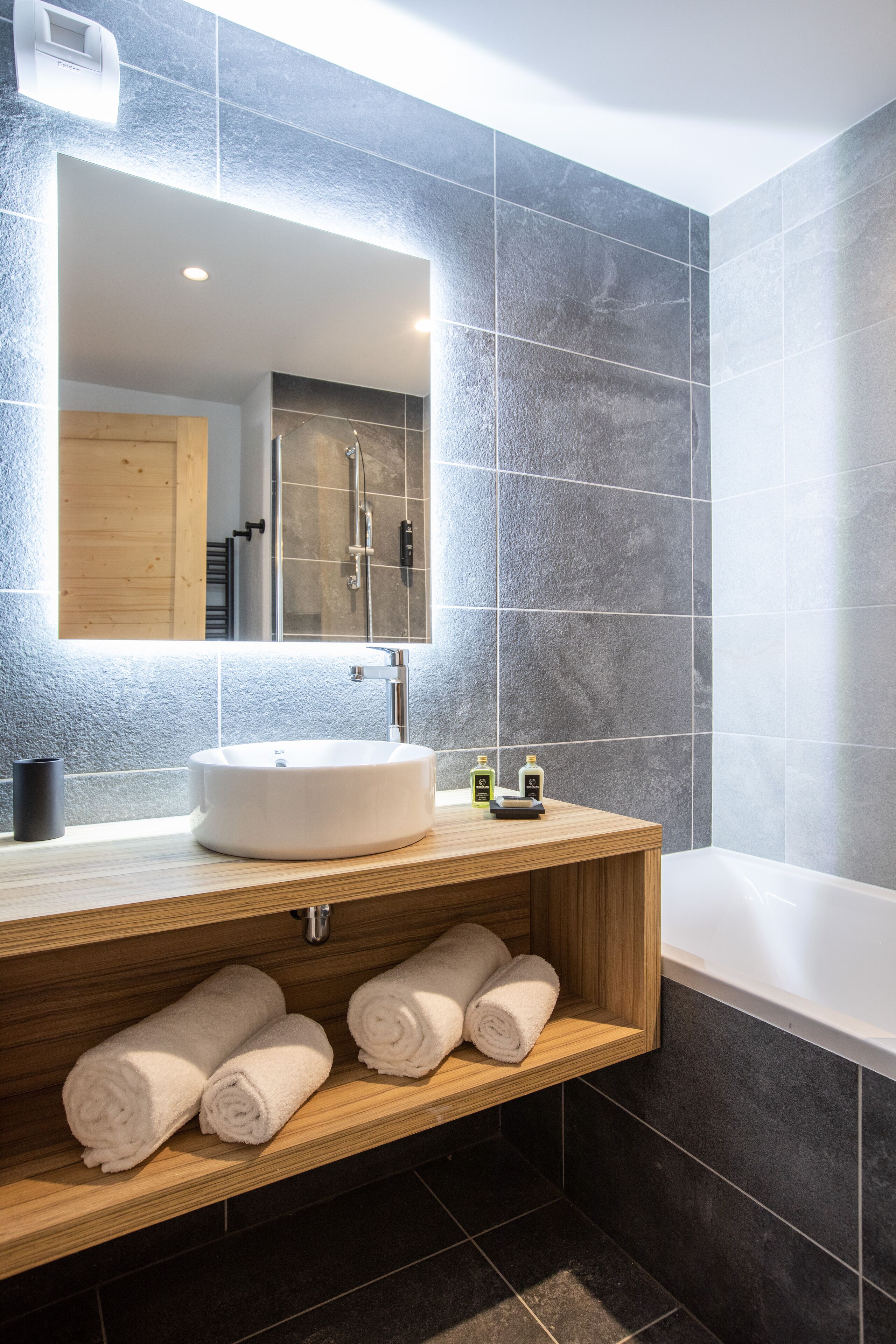 Une salle de bain moderne avec un grand miroir, un lavabo rond et un meuble-lavabo en bois.