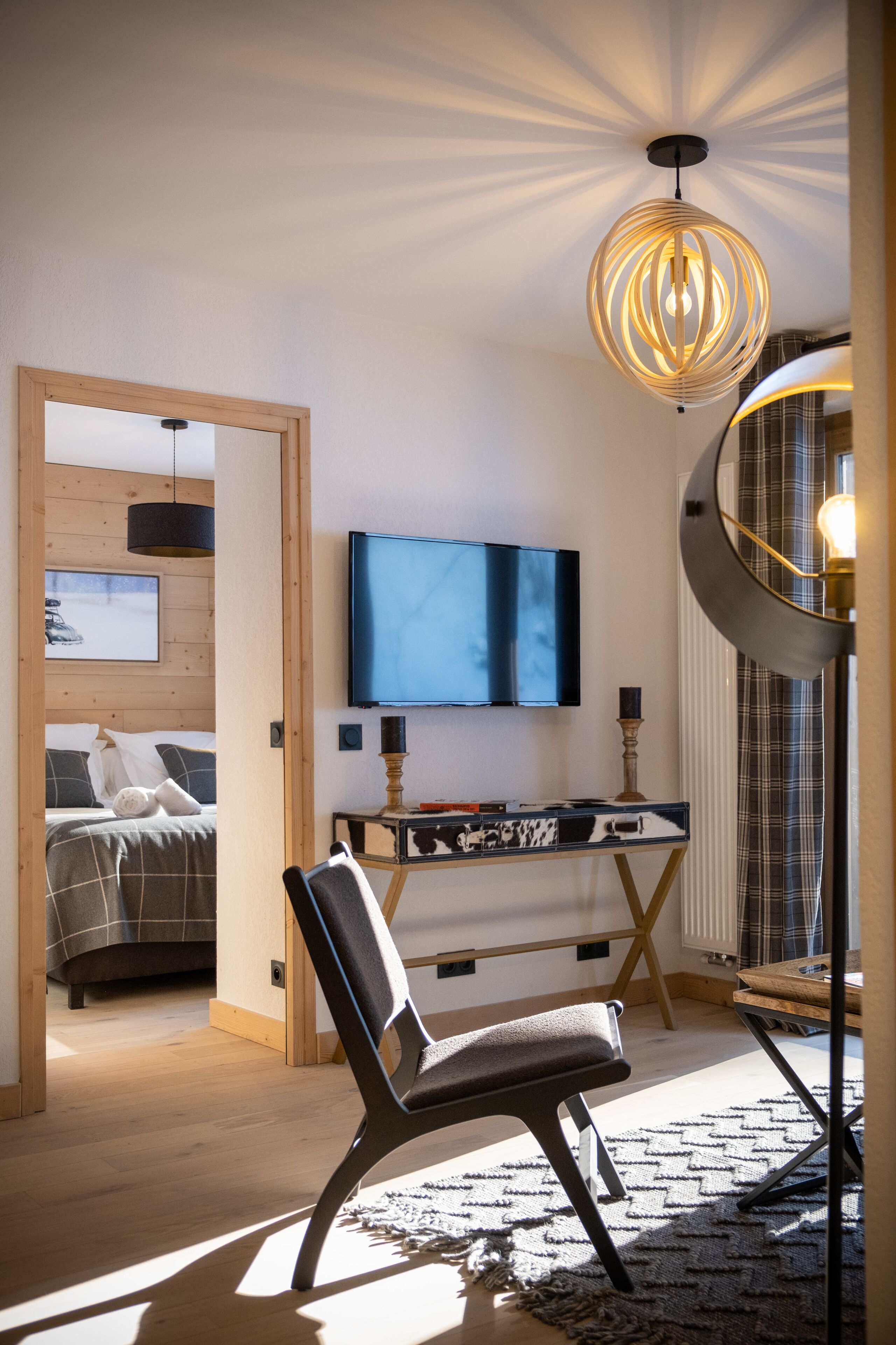 A modern bedroom with a bed, a desk, a chair, a television, and a unique ceiling light fixture.