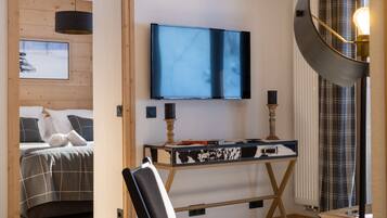 A modern bedroom with a bed, a desk, a chair, a television, and a unique ceiling light fixture.