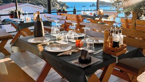 Una mesa dispuesta para comer, con vistas al mar, muebles de madera y botellas de vino.