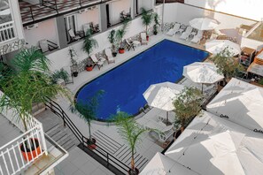 Un espace piscine aménagé sur le toit, avec des chaises longues, des parasols et des plantes en pot.