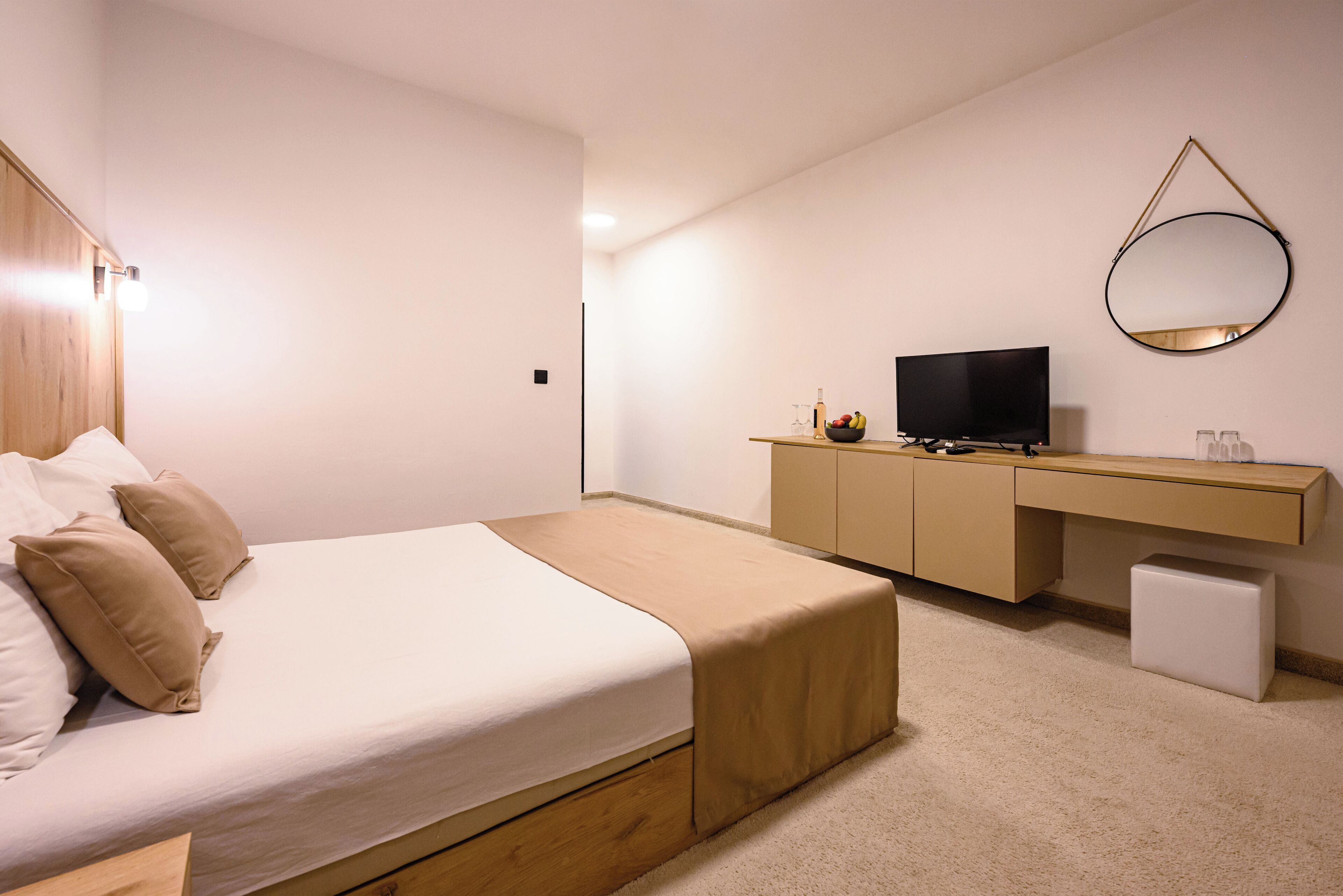 A bedroom with a bed, a desk, a television, a mirror, and a small white cabinet.