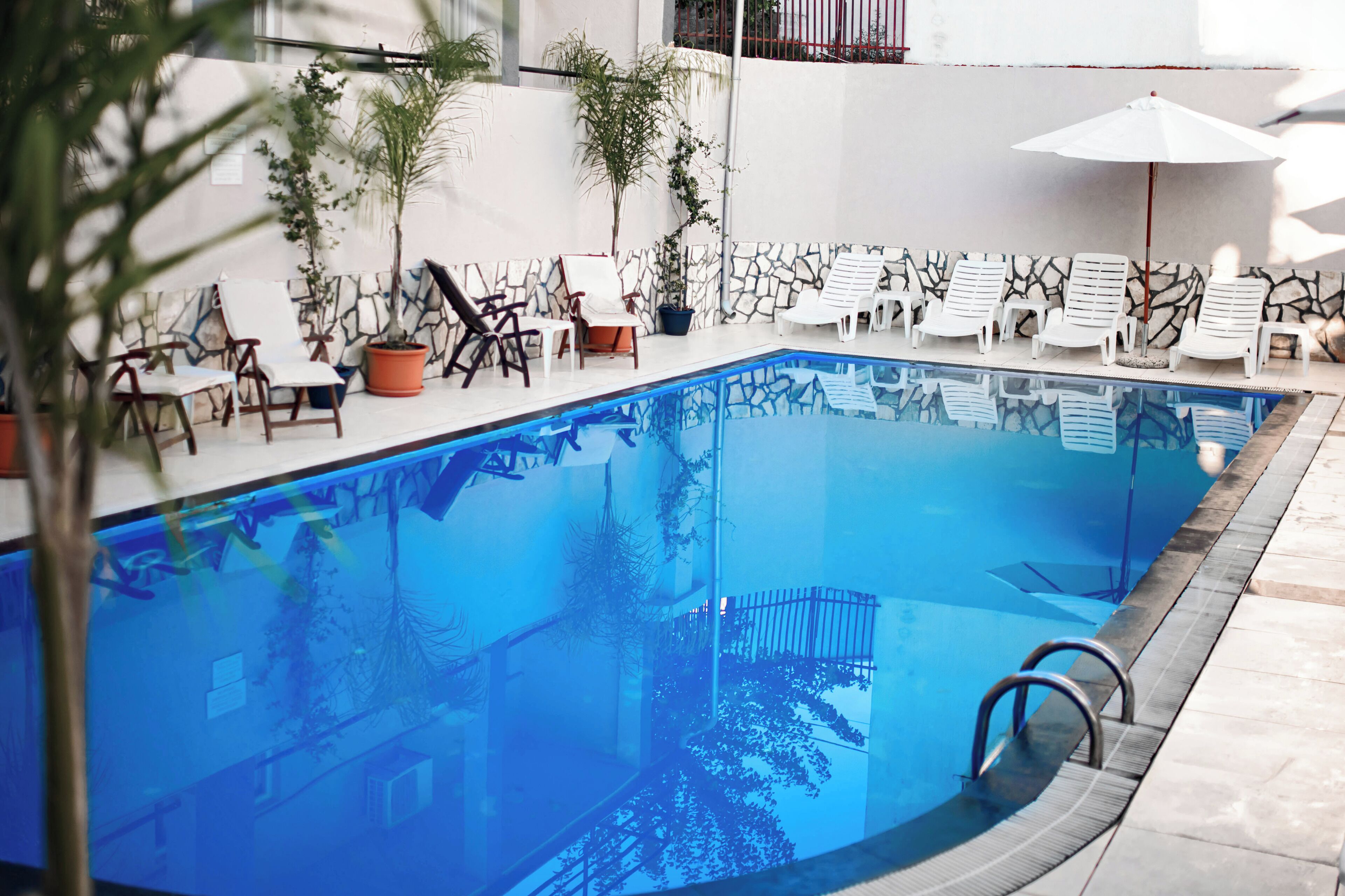 An indoor swimming pool with lounge chairs and umbrellas, surrounded by potted plants and a stone wall.