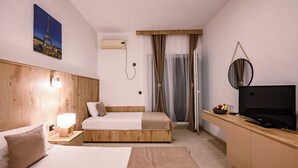 Habitación de hotel con cabecera de madera, cama con ropa de cama blanca, mesita de noche con lámpara, televisor de pantalla plana y frutero.