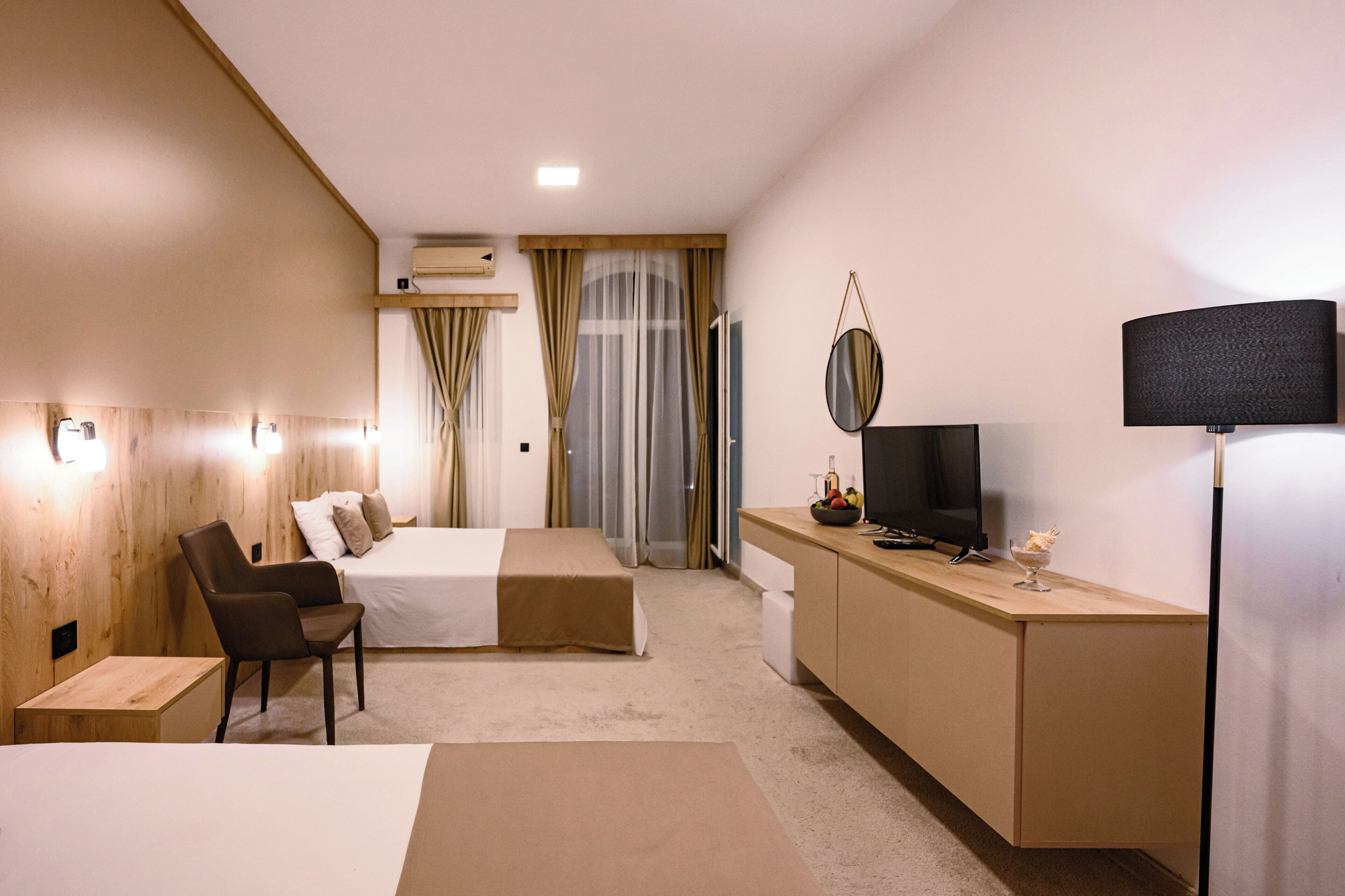 A hotel room with a bed, a desk with a TV, a chair, and a small table with a bowl of fruit.