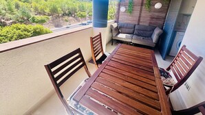 A balcony with a wooden table and chairs, a sofa, and a view of a green landscape.