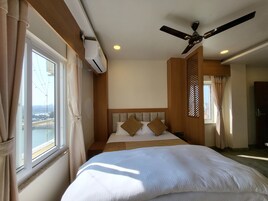 Habitación de hotel con cama, ventilador de techo, aire acondicionado, ventana con cortinas y vista a un paisaje urbano.