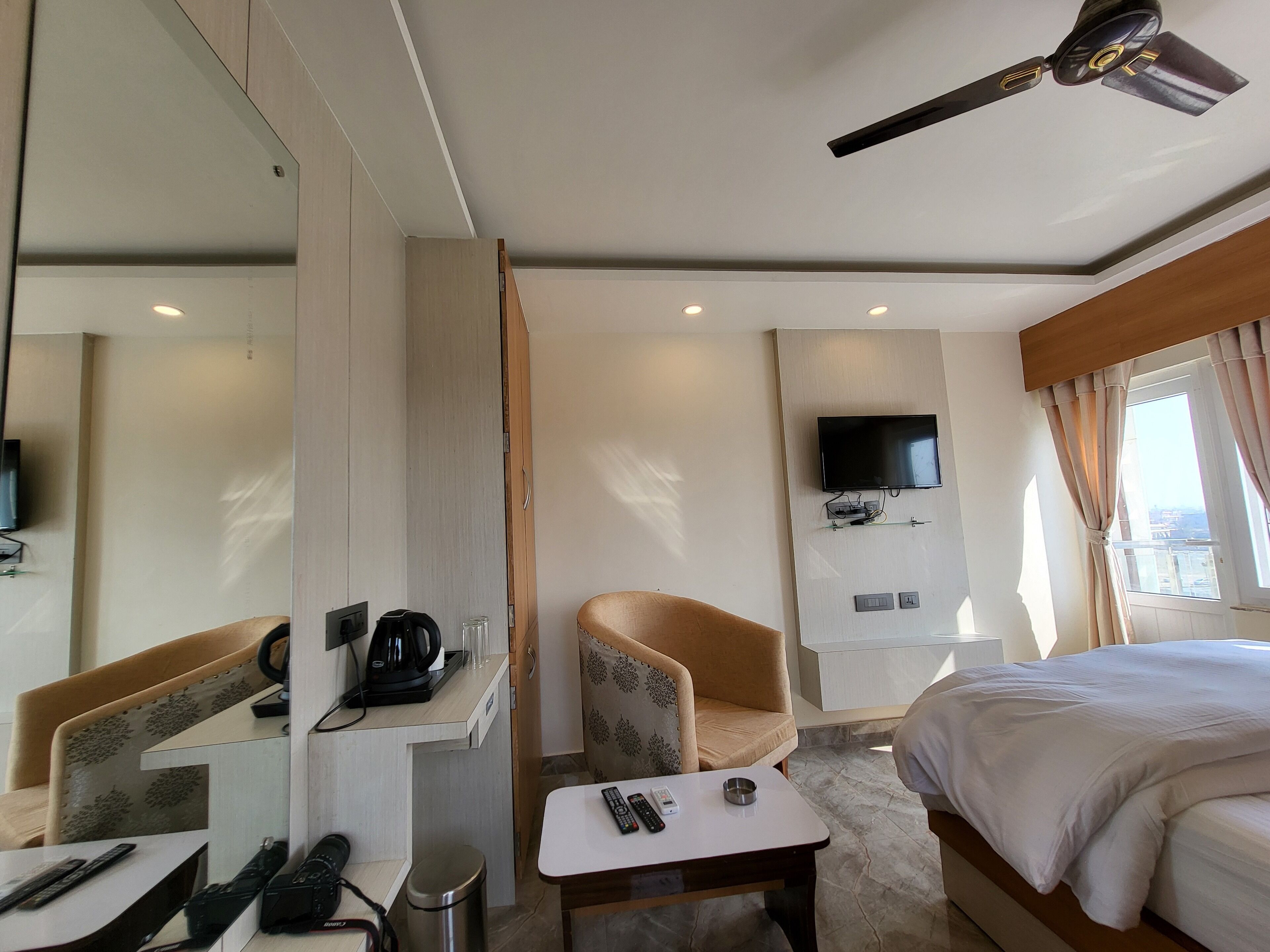 Ein Hotelzimmer mit einem Bett, einem Sofa, einem kleinen Tisch mit Fernbedienung, einer Kaffeemaschine und einem an der Wand befestigten Fernseher.