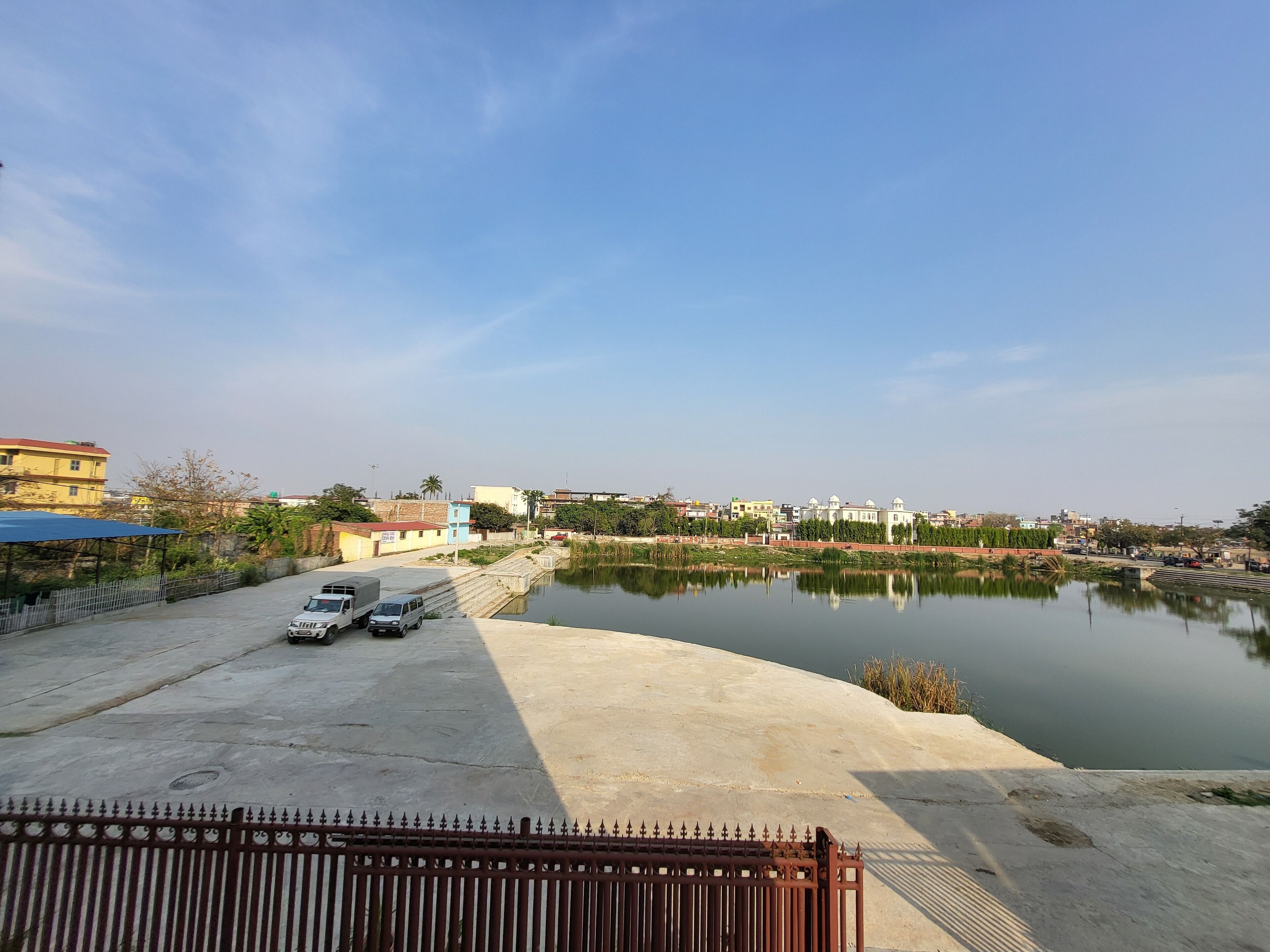 A calm river with a concrete embankment and a metal fence in the foreground.