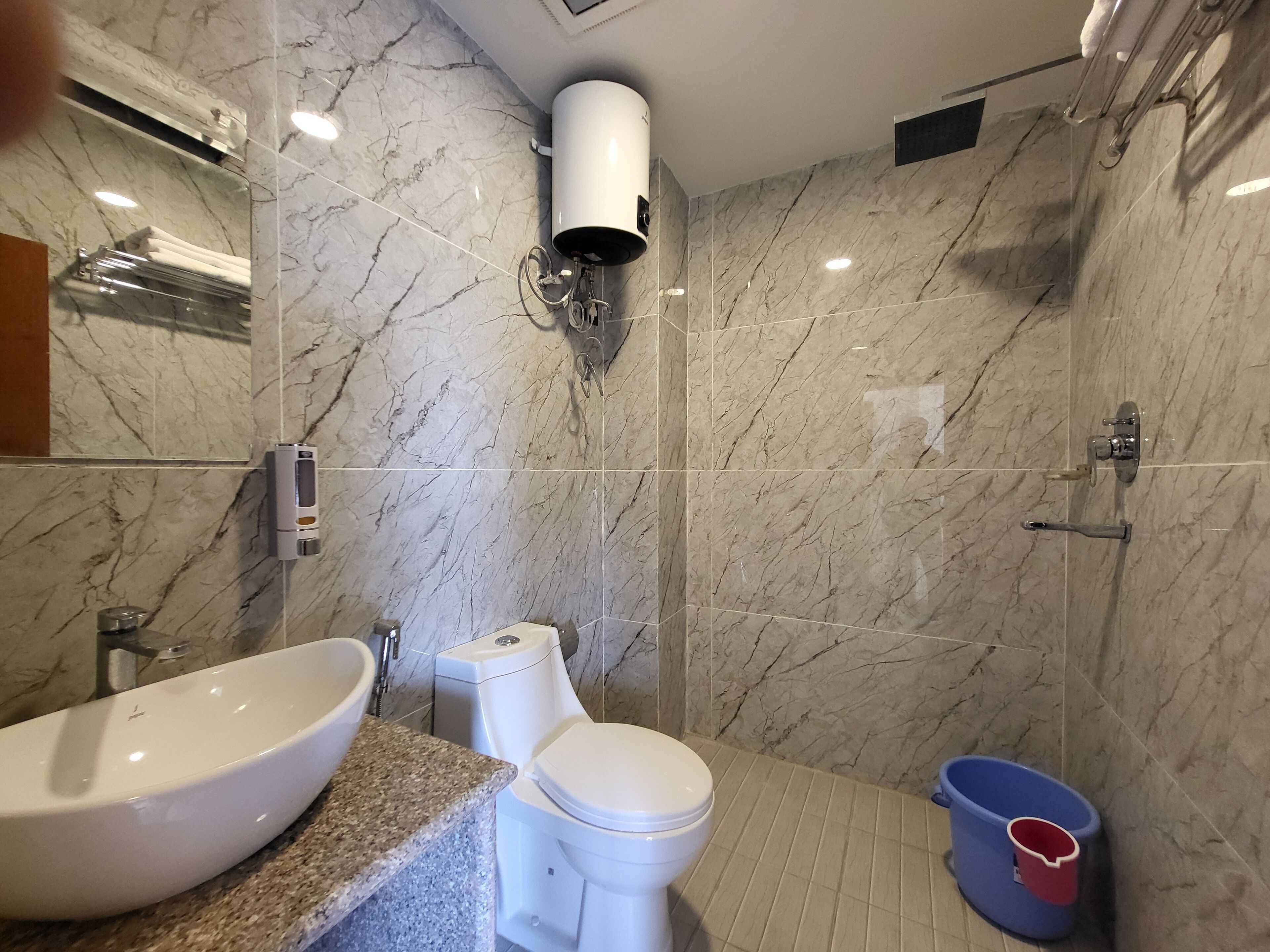 A modern bathroom with a marble wall, a large sink, a toilet, and a shower area.