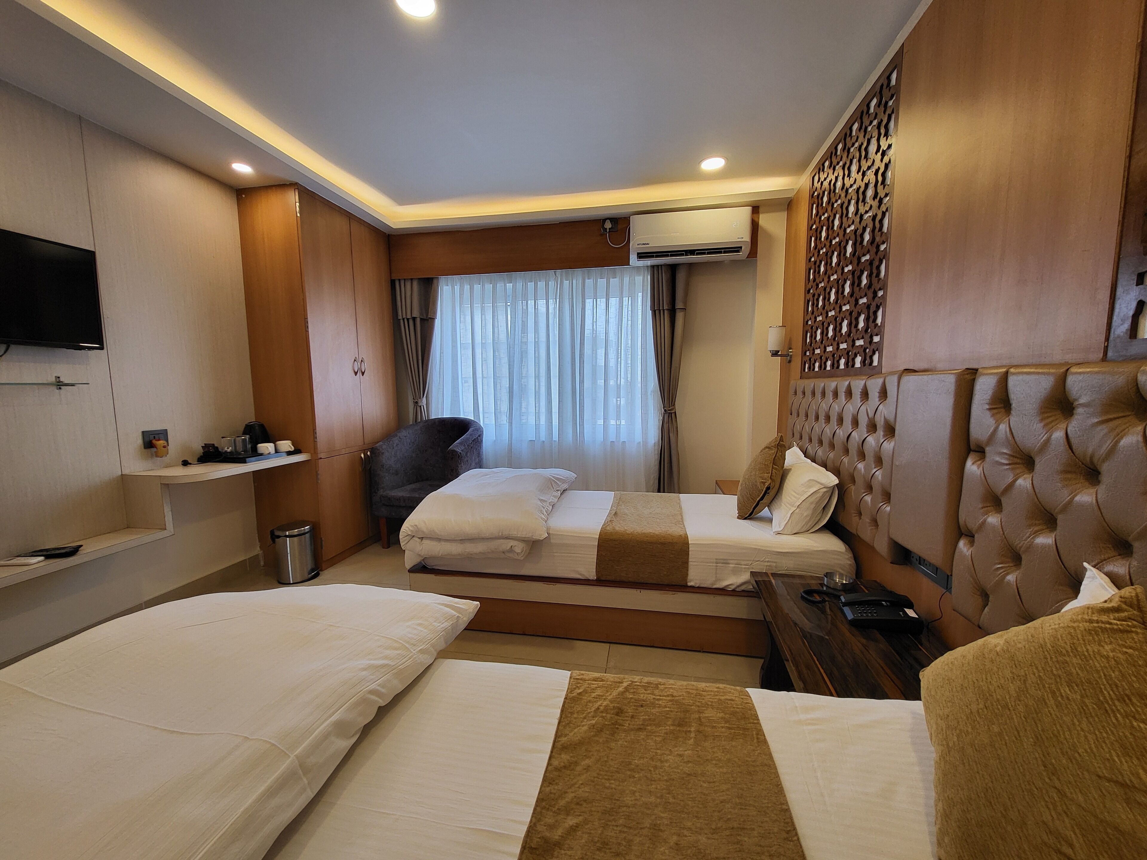 Habitación de hotel con dos camas, un televisor, un armario, un escritorio y un aire acondicionado.