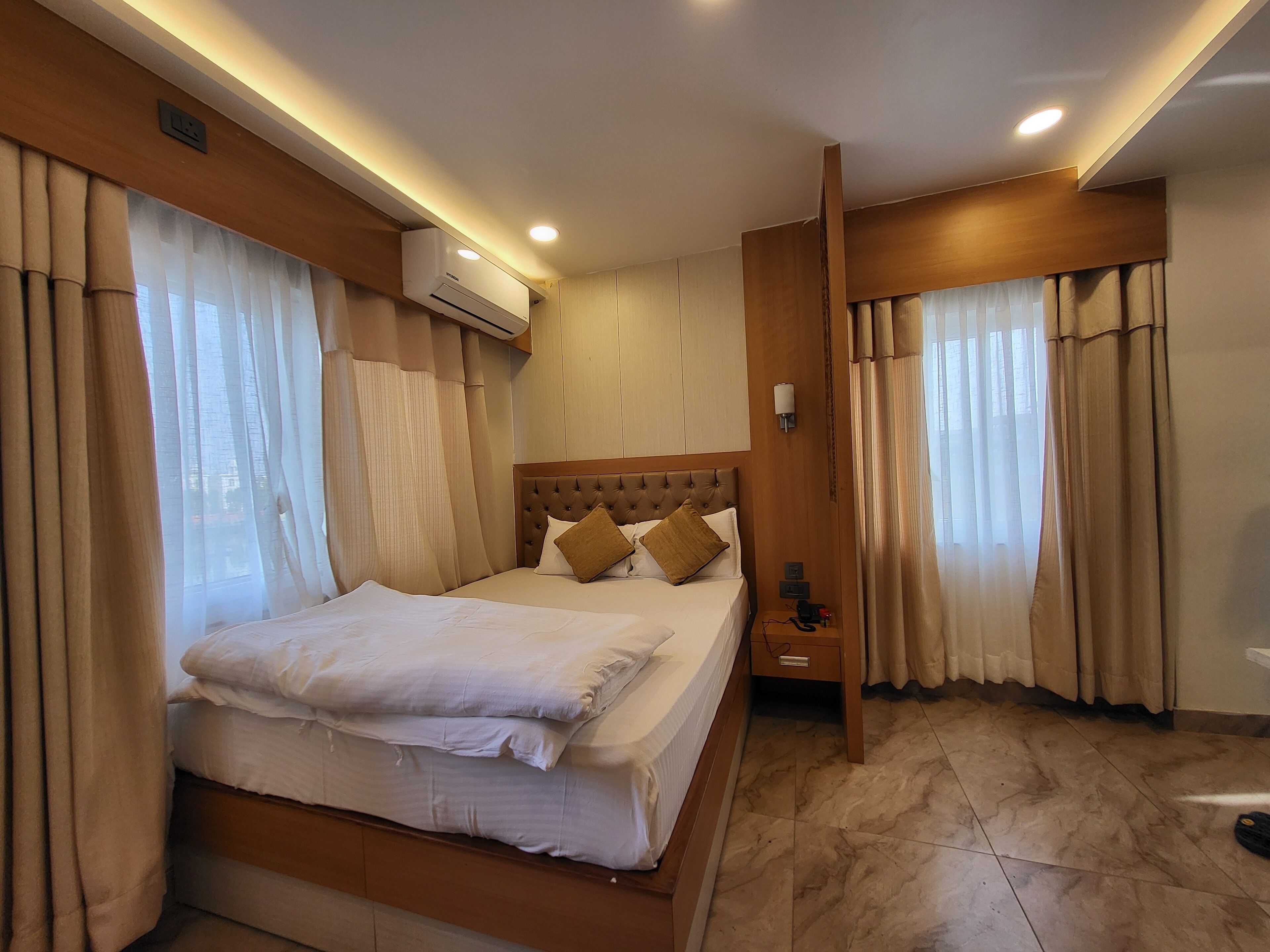 Una cama bien hecha con un cabecero de madera, una mesita de noche con una lámpara y un aire acondicionado de pared.