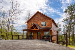 A wooden cabin with a porch and a fenced driveway.