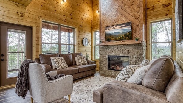 Ein gemütliches Blockhaus-Interieur mit Kamin aus Stein, Ledersofas und großen Fenstern mit Blick auf den Wald.