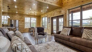 Ein geräumiges Holzhaus-Interieur mit Wohnbereich, Esstisch und großen Fenstern, die einen Blick ins Freie bieten.