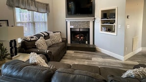Una sala de estar con chimenea, televisor montado encima y un conjunto de sofás.