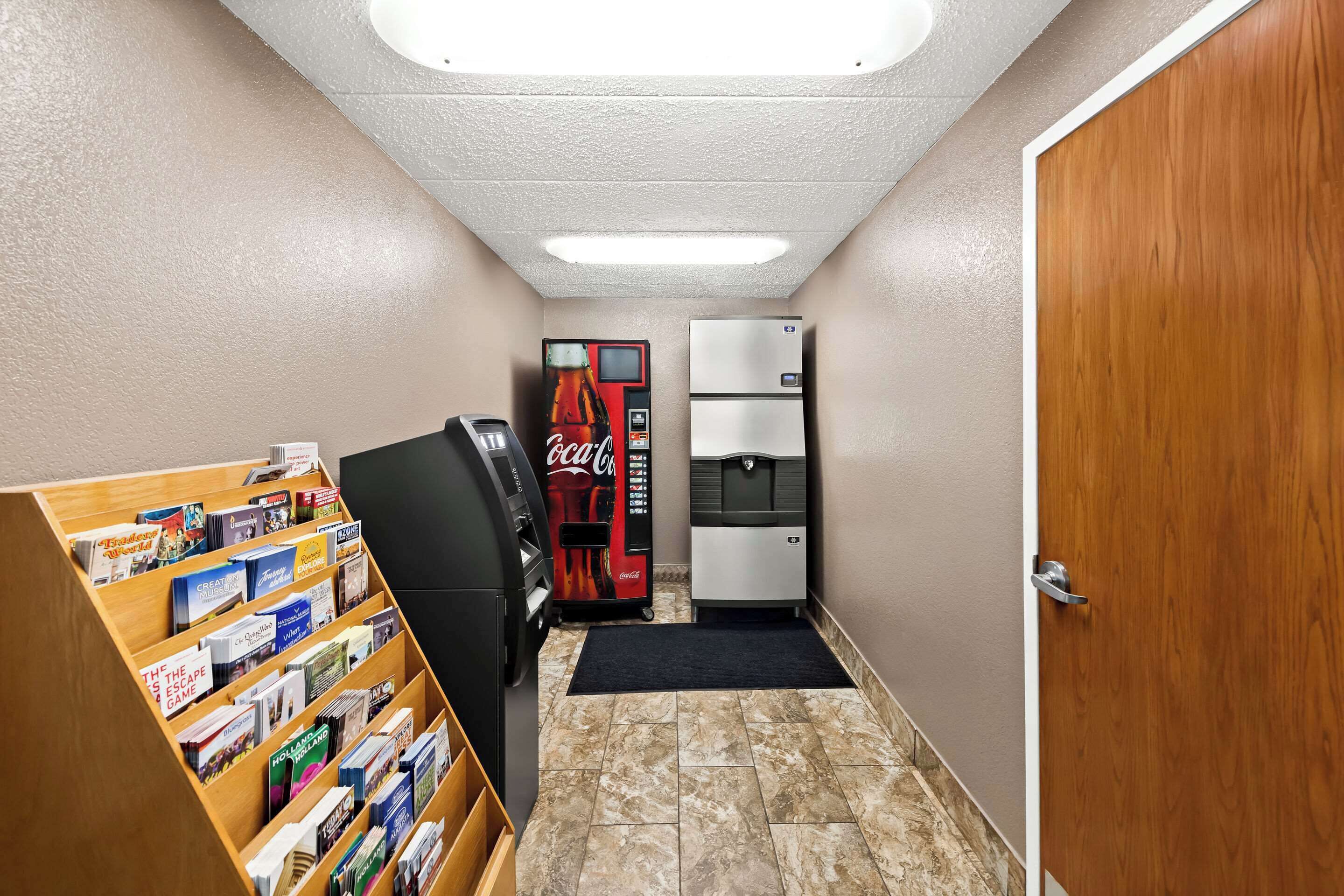 A hallway with a vending machine, a refrigerator, and a bookcase filled with books.