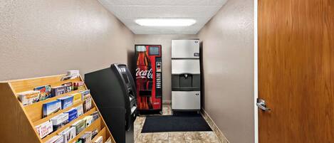 A hallway with a vending machine, a refrigerator, and a bookcase filled with books.