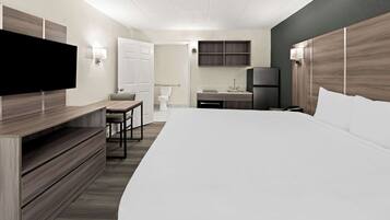 A modern hotel room with a large bed, a desk, a TV, and a small kitchenette.