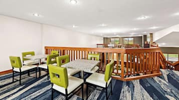 A hotel dining area with a high wooden railing, multiple tables and chairs, and a view of the outdoors through large windows.