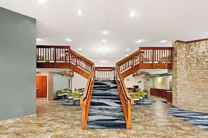 A hotel lobby with a central staircase, multiple dining areas, and a reception desk.