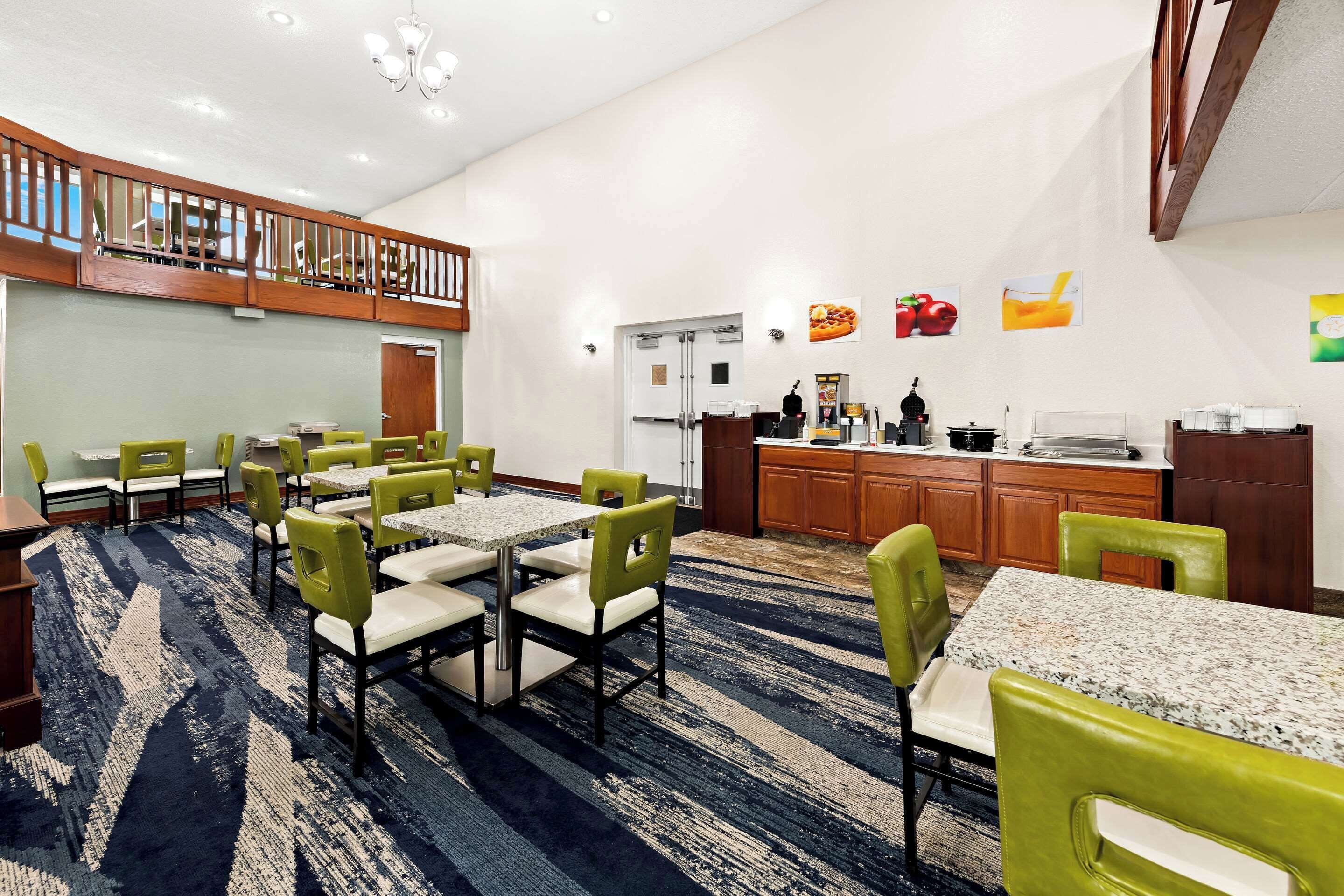 Un comedor de hotel con varias mesas y sillas, una cocina al fondo y un balcón con barandillas de madera.