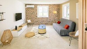 A modern living room with a brick wall, a grey sofa, a round coffee table, and wicker chairs. - Charming cottage with spa and terrace in vineyards (Saulcet)