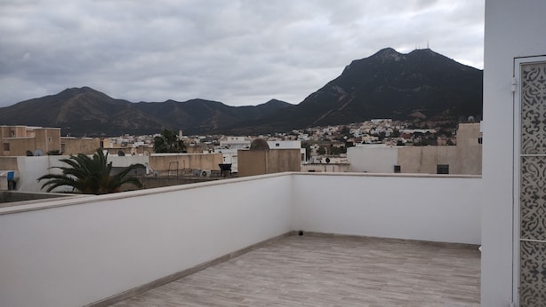 A rooftop terrace with a view of a mountain range and a town below. - Hammam lif Apartment Magnificent Mountain View (Hammam-Lif)