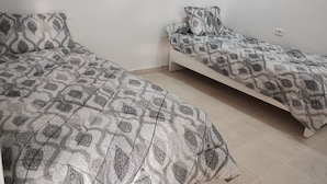 Two single beds with patterned bedding in a room with plain walls and a tiled floor. - Hammam lif Apartment Magnificent Mountain View (Hammam-Lif)